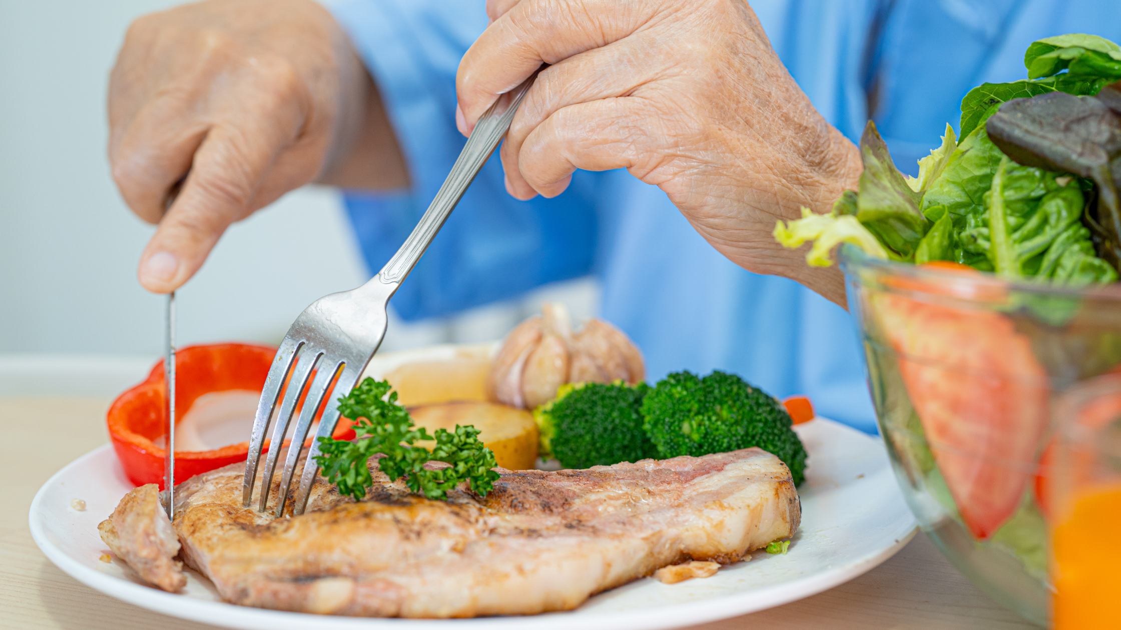 photo of a person's hands holding a fork and knife and slicing a pork chop on a plate of vegetables