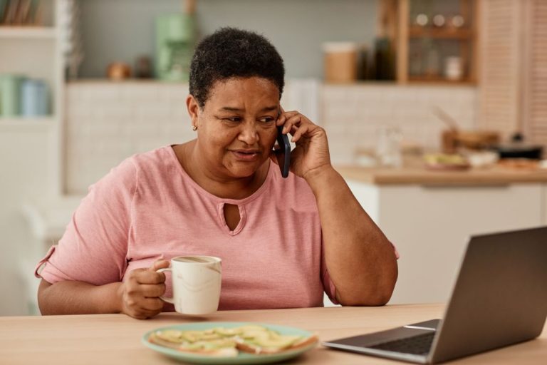Warm toned portrait of senior woman talking on phone while enjoying breakfast in morning